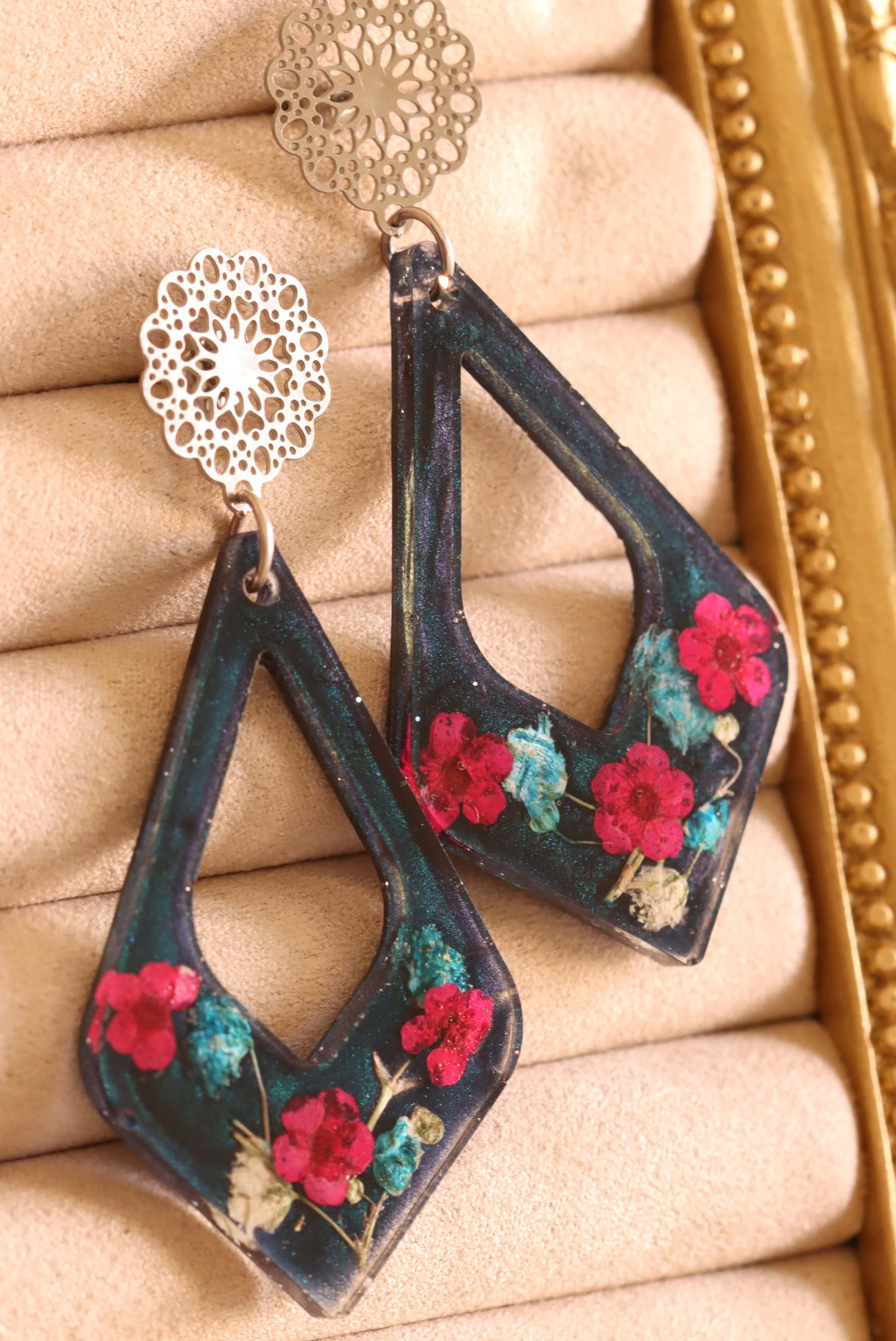 Close-up of the Floral Romance Resin Earrings - part of the Gothic Romance Jewelry Collection by Kaleidoscopes And Polka Dots. These earrings feature a midnight blue background and are displayed on a beige jewelry tray with gold trim.