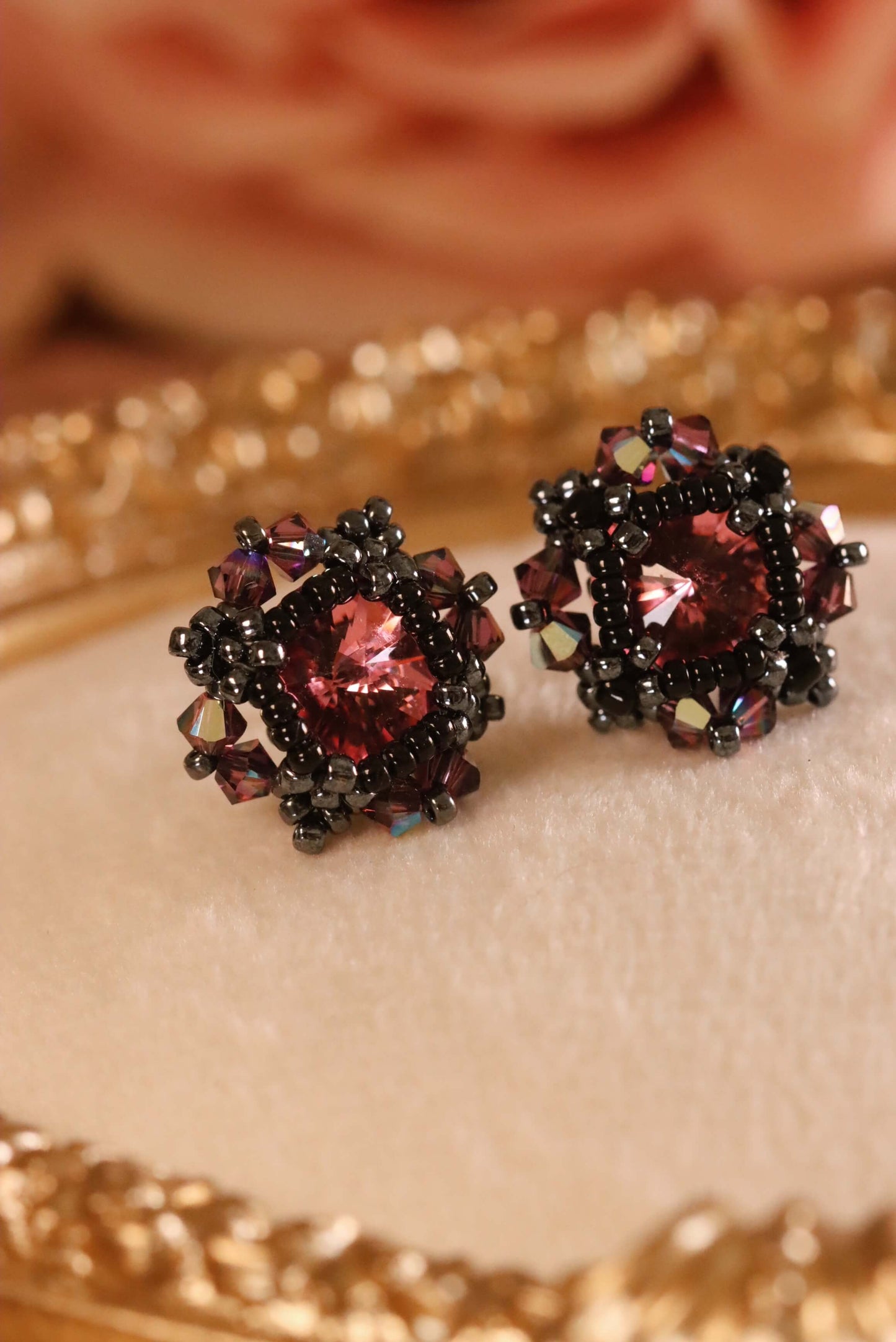 Pair of ornate gothic stud earrings with pink crystals surrounded by delicate black beading set against a textured surface