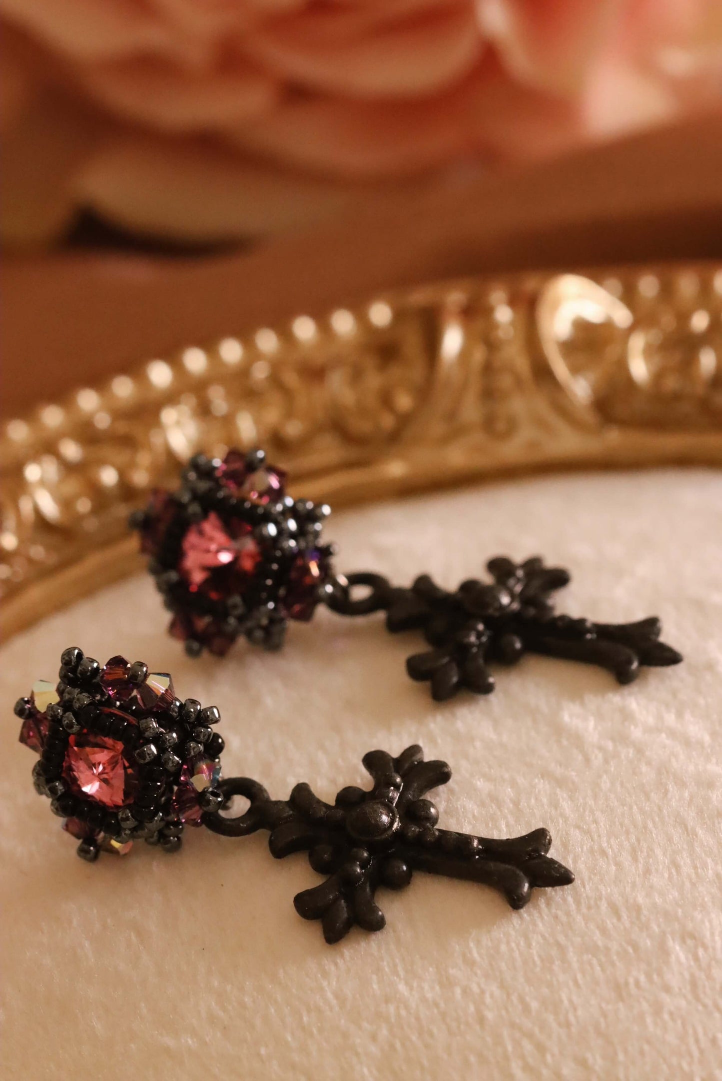 Pair of Gothic Cross Crystal earrings with black cross charms and pink crystals on a decorative plate