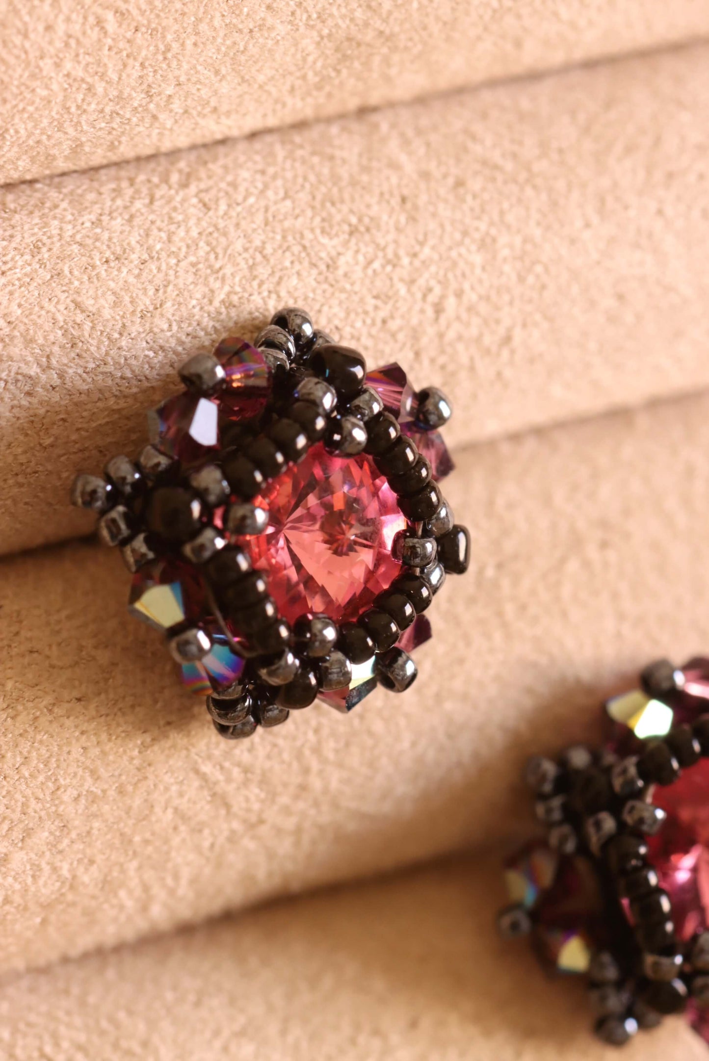 Close-up of a decorative beaded stud earring with pink and purple crystals and black beads on a beige surface