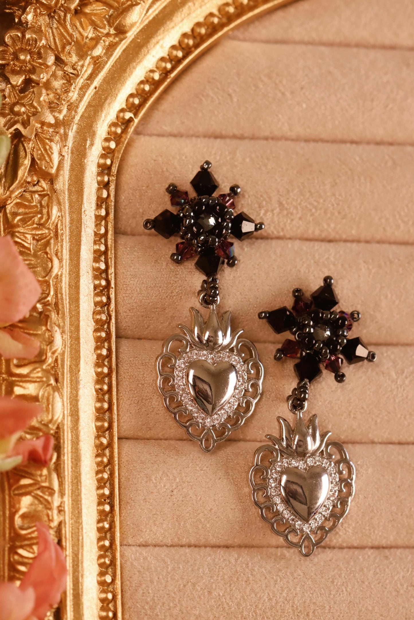Sacred Heart Drop Earrings - a close-up of he front detail of these beaded crystal earrings. These drop earrings are part of the Gothic Romance Jewelry Collection. These stud earrings are set against a beige backdrop in a jewelry display.