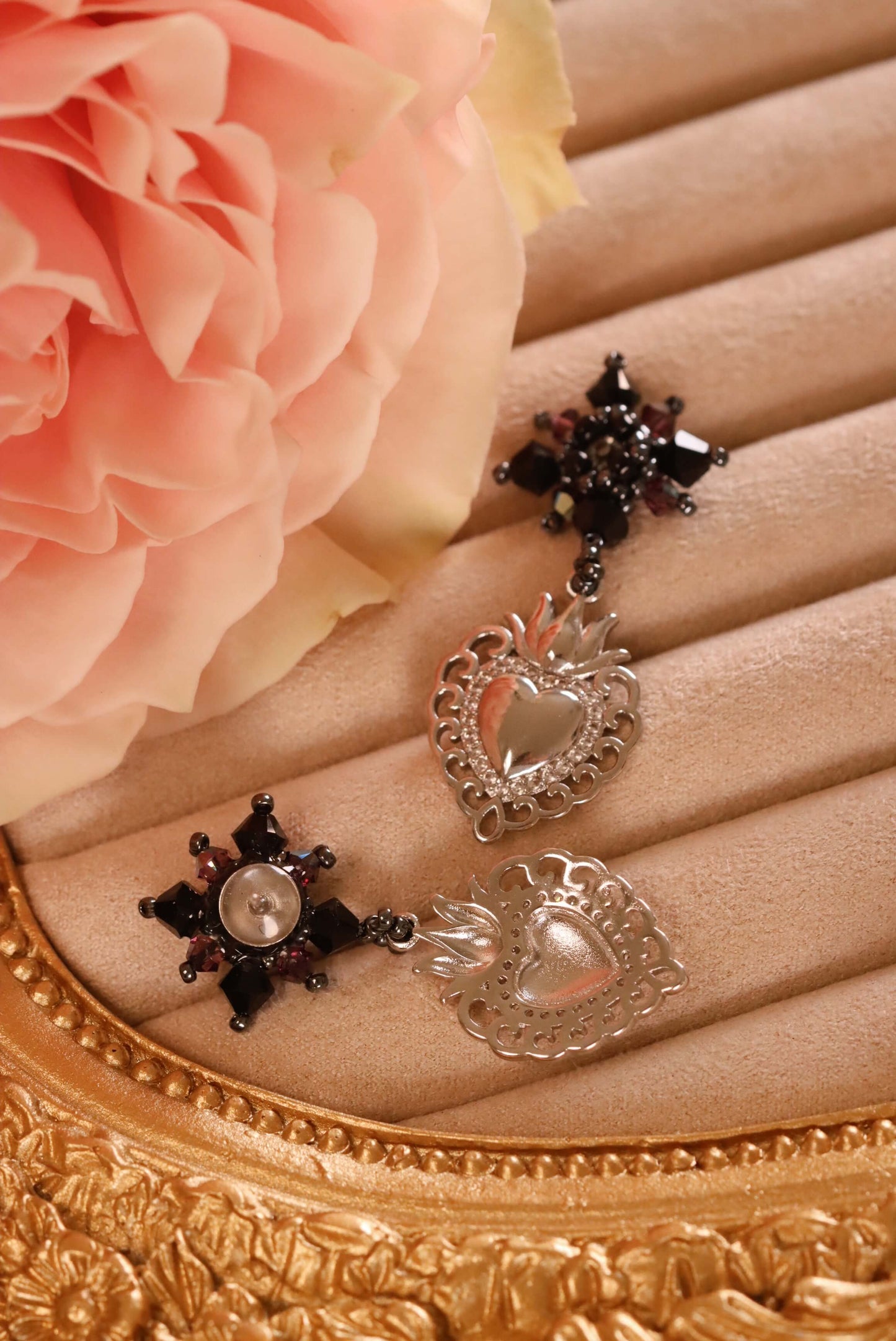 Sacred Heart Drop Earrings - a close-up of the front and back of these earrings, which are part of the Gothic Romance Jewelry Collection. These stud earrings are set against a beige jewelry display and a pink rose.