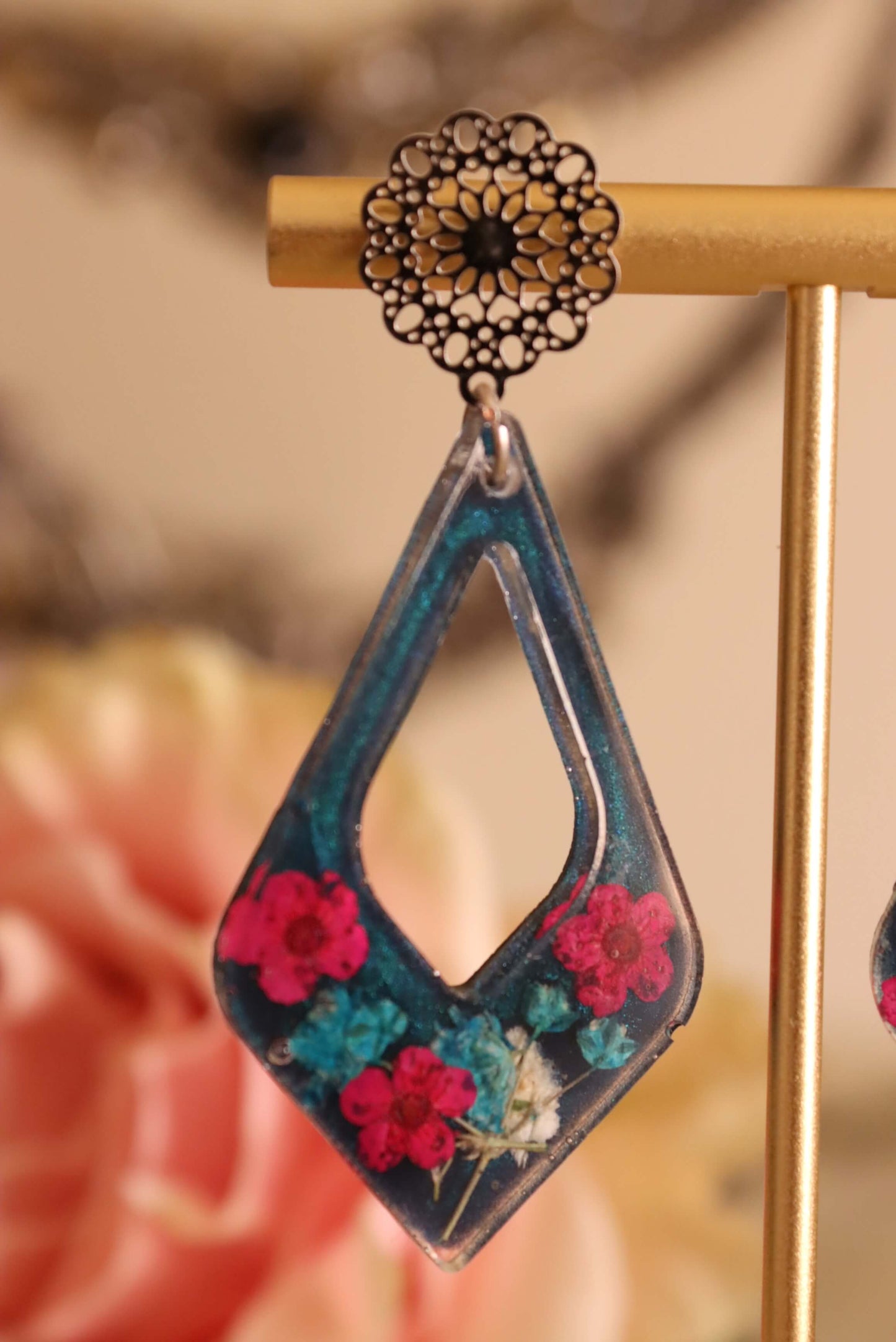 Close-up of the Floral Romance Resin Earrings - part of the Gothic Romance Jewelry Collection by Kaleidoscopes And Polka Dots. These earrings feature a midnight blue background and are displayed against a floral blury background.