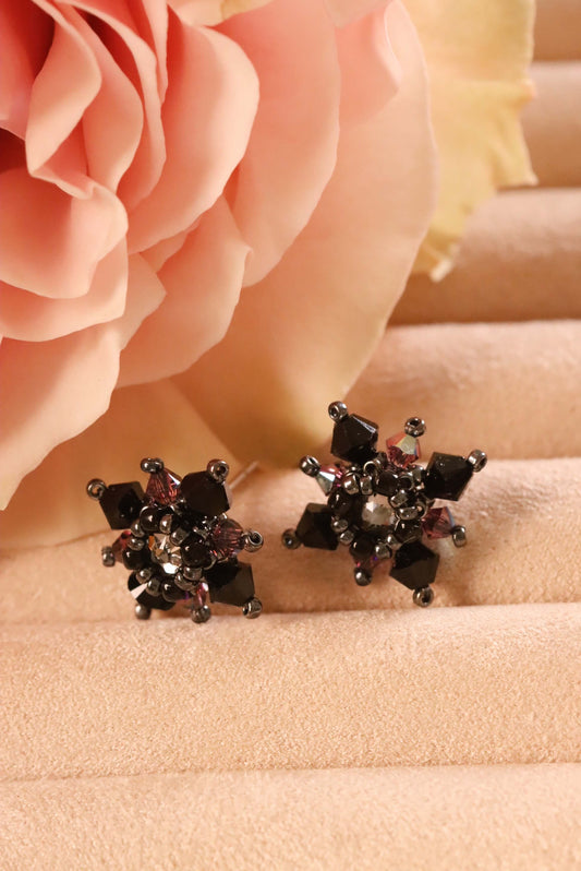 Front view of Gothic Stud Earrings from the Gothic Romance Jewelry Collection set against a beige jewelry display and a pink rose. 
