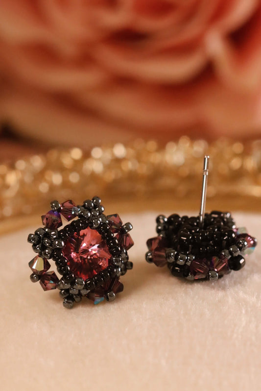 Pair of beaded gothic stud earrings  with a pink focal crystal center and with a blurred rose in the background