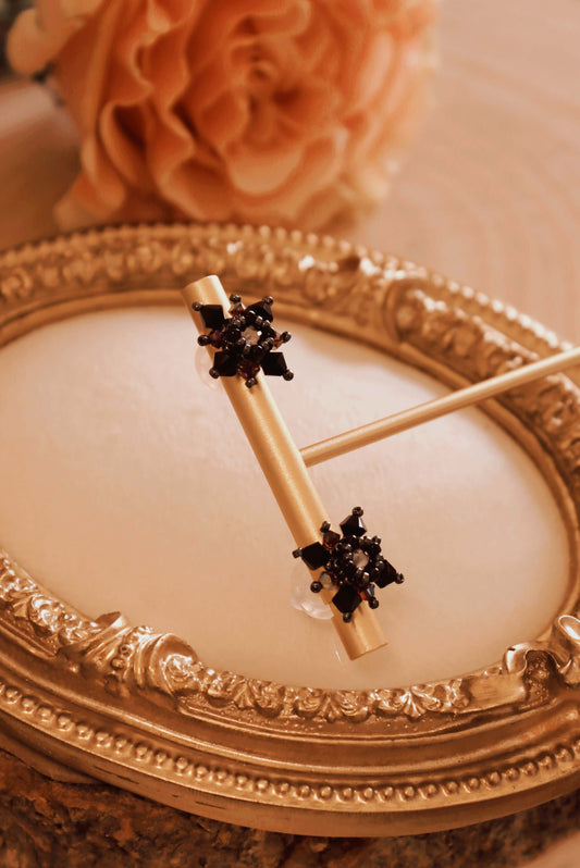 Side view of Gothic Stud Earrings from the Gothic Romance Jewelry Collection set against a beige jewelry tray and a pink rose. These stud earrings are shown on a gold t-bar earring display.