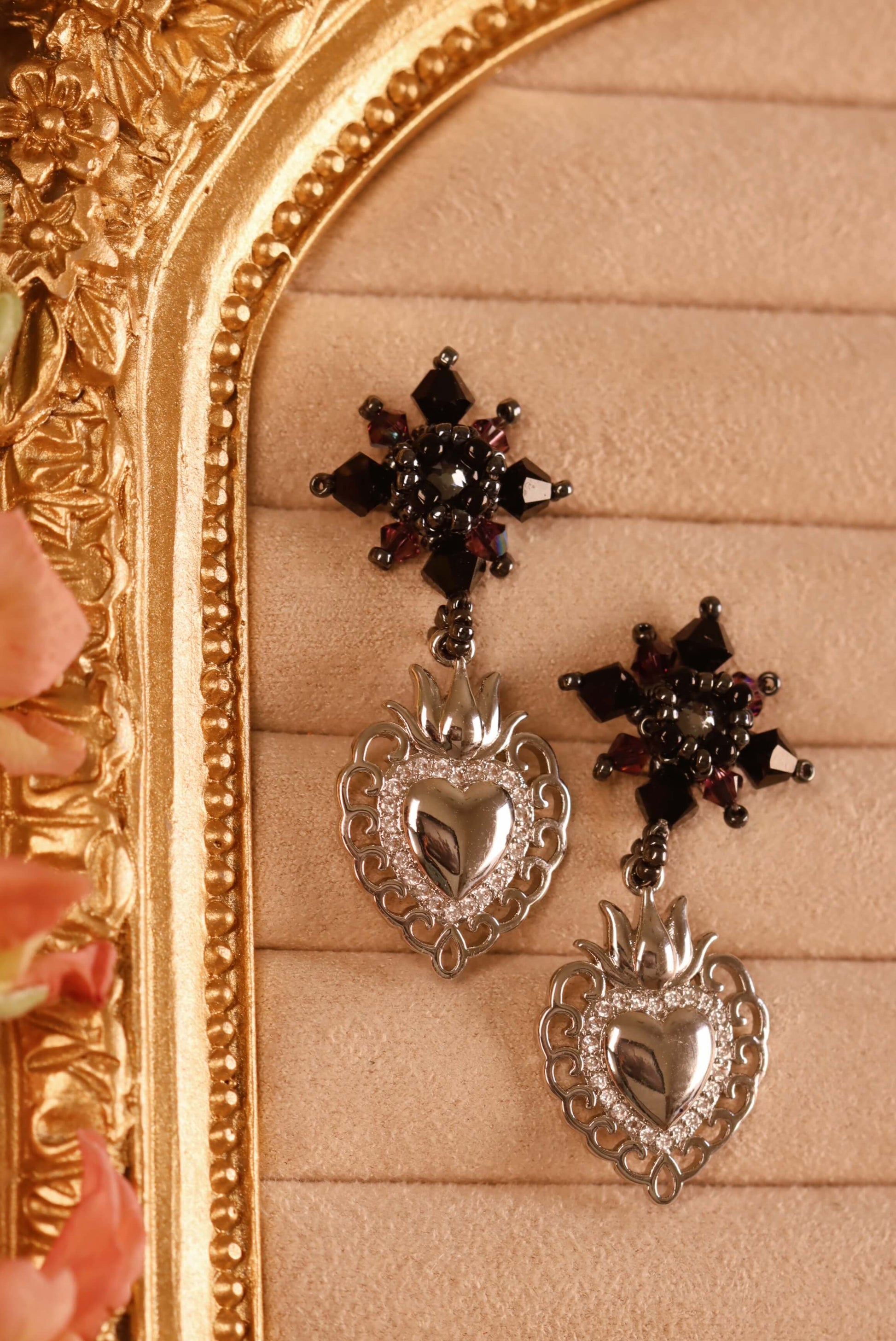Sacred Heart Drop Earrings - a close-up of he front detail of these beaded crystal earrings. These drop earrings are part of the Gothic Romance Jewelry Collection. These stud earrings are set against a beige backdrop in a jewelry display. 